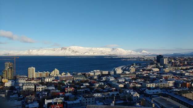 Aerial shot of the coastal city of Reykjavik with snow covered mountains against a blue sky