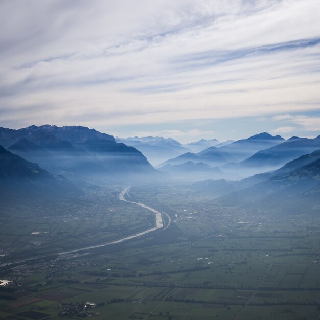 Aerial shot of a curvy road towards the mountains in fog under a cloudy sky