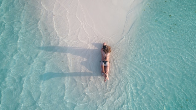 Aerial shot of a girl laying on the sand and tanning at the beach