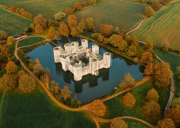 Aerial shot of a magnificent old castle in the middle of a lake surrounded by trees and farms