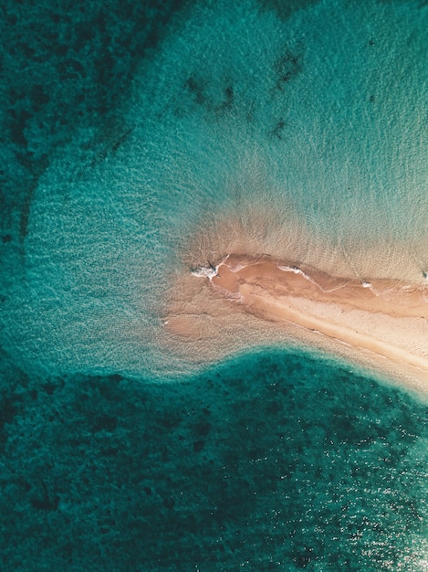 Aerial shot of the ocean waves hitting the small sandy island