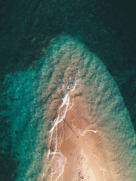 Aerial shot of the ocean waves hitting the small sandy island