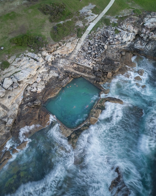 Aerial shot of people swimming in a large pool built on the rocky coast in Thailand