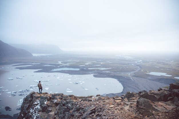 Aerial shot of a person standing on a cliff overlooking the lakes in the fog captured in Iceland