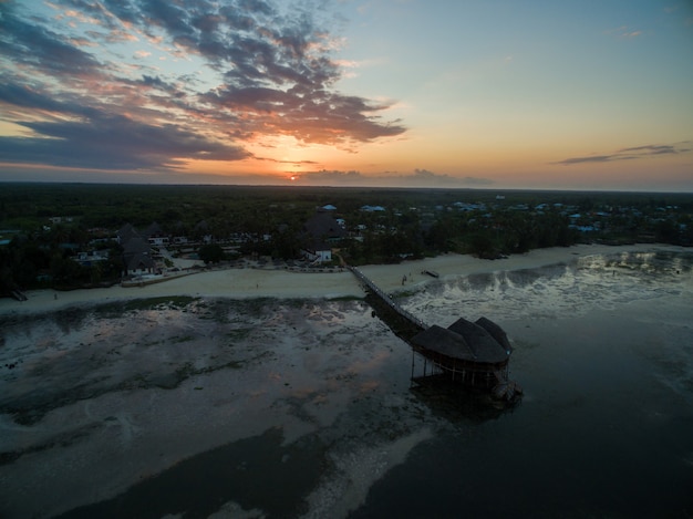 ザンジバル、アフリカの夕日の下でキャプチャされた海沿いのビーチで桟橋の空中ショット