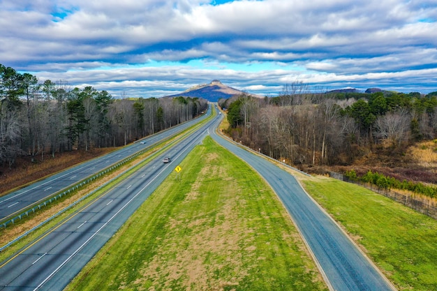 Aerial shot of a road with Pilot mountain in North Carolina, USA and a cloudy blue sky