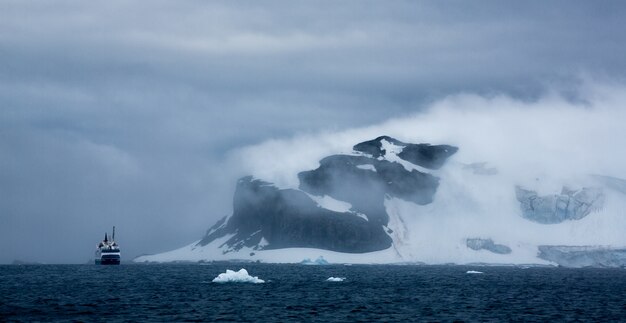 Aerial shot of a ship and iceberg in Antarctica under cloudy sky