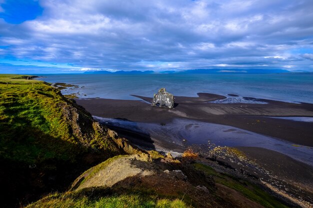 Aerial shot of the shoreline near a grassy hill under a cloudy sky