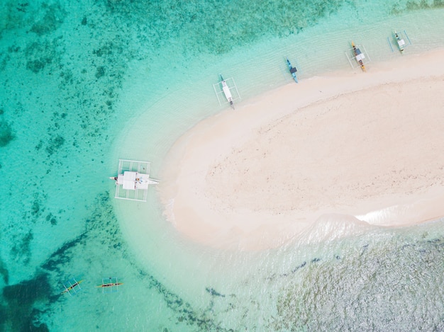 Aerial shot of a small sandy island surrounded by water with a few boats