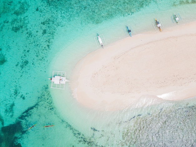 Аэрофотоснимок небольшого песчаного острова, окруженного водой, с несколькими лодками