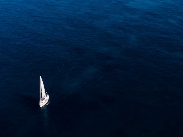 Aerial shot of a small white boat sailing in the ocean