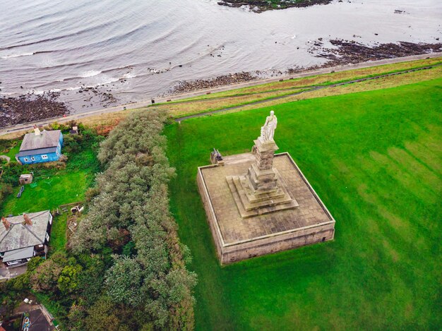 Aerial shot of a statue in the green valley near the sea