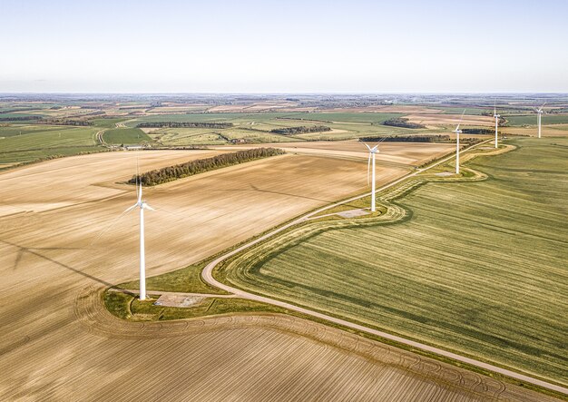 Aerial shot of the turbines on the beautiful green fields near the plowed farms