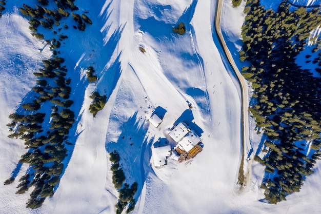 Aerial top view of small houses on a snowy mountain surrounded by trees in the daylight