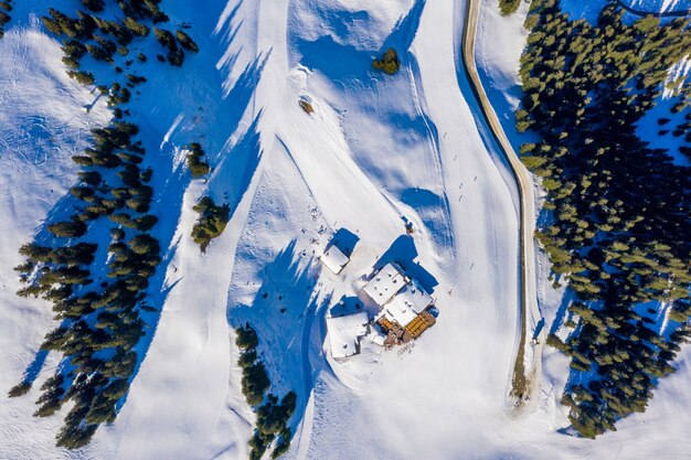 Aerial top view of small houses on a snowy mountain surrounded by trees in the daylight