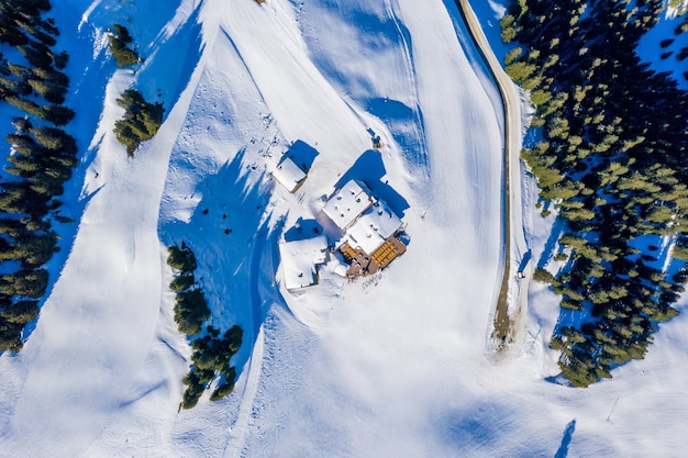 Aerial top view of small houses on a snowy mountain surrounded by trees in the daylight