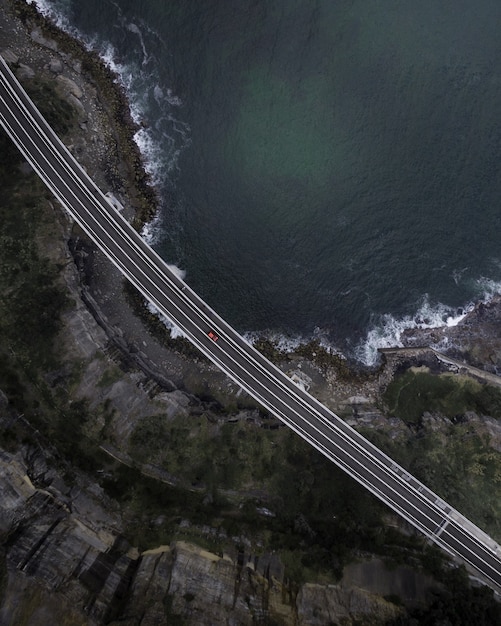 Aerial top view of a straight paved highway road with a single car running along the seashore