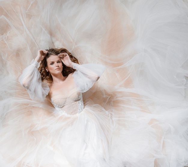 Aerial view of beautiful young bride lying on the ground and looking at the camera, all around in chiffon