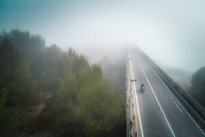 Aerial view of a biker crossing a bridge covered with fog