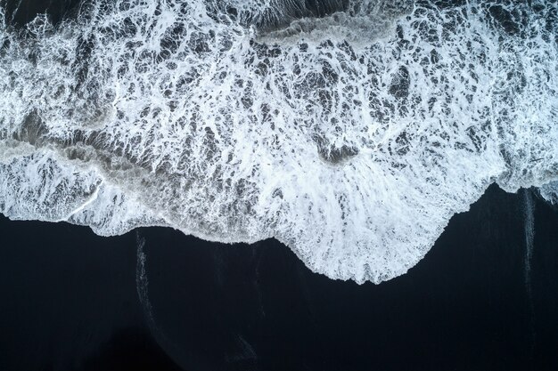 Вид с воздуха на пляж с черным песком и океанские волны в Исландии.