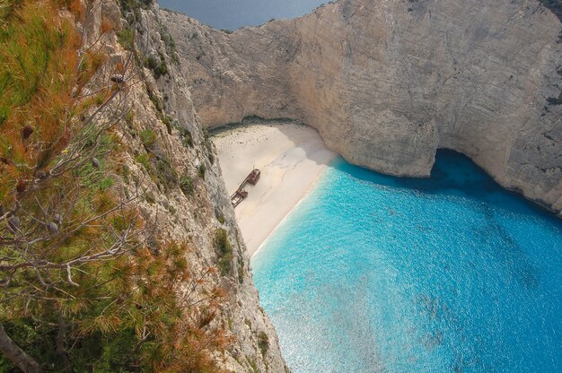 Aerial view of the blue ocean surrounded by cliffs with the remnants of an old boat in the shore