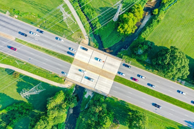 小川に架かる橋と道路上の車のある送電線の航空写真