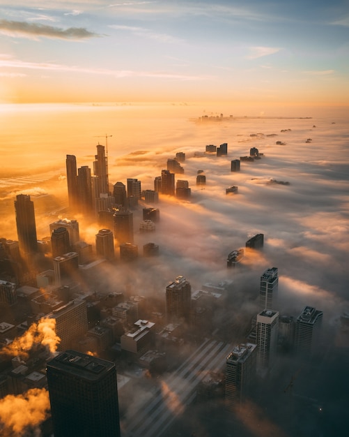 Aerial view of a cityscape with tall skyscrapers during sunset covered with white clouds