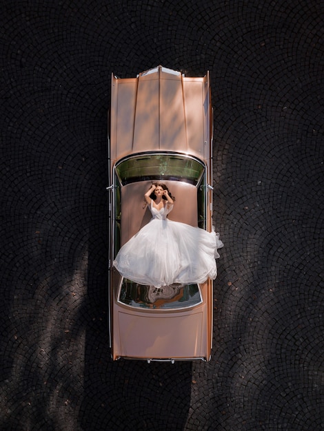 Free photo aerial view of elegant bride lying on the roof of a pink retro car