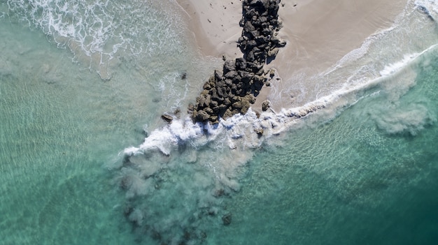Aerial view of the ocean waves breaking by the pile of rocks on the beach