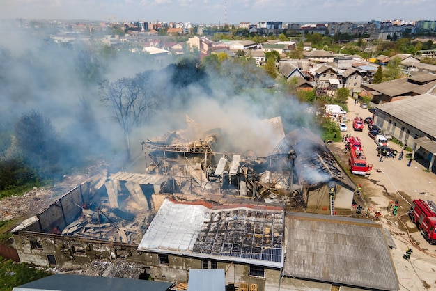 崩壊した​屋根​と​上昇する​暗い​煙​で​火事​で​廃墟​の​建物​を​消火する​消防士​の​航空​写真​。