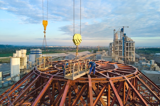 Вид с воздуха рабочих на строящемся цементном заводе с высокой структурой бетонного завода и башенными кранами в зоне промышленного производства.