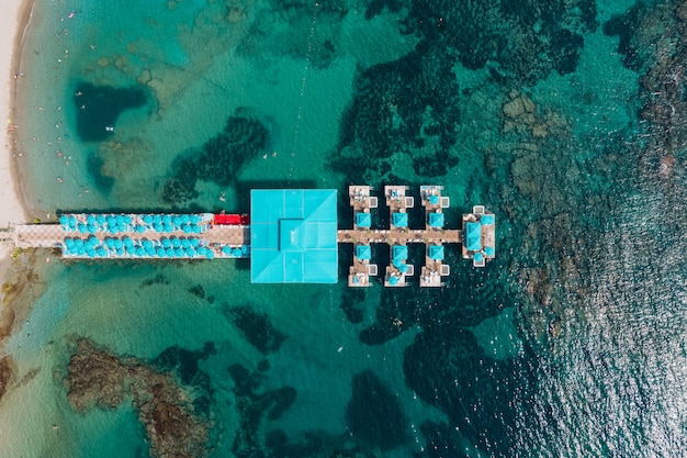 Вид с воздуха на курортный пирс в прозрачной морской воде с камнями