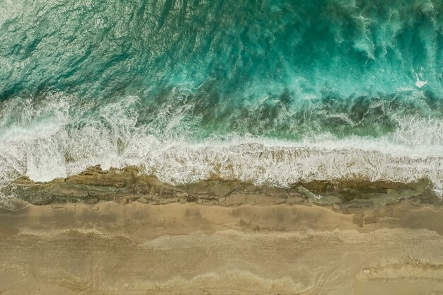 Аэрофотоснимок песка, встреча морской воды и волн