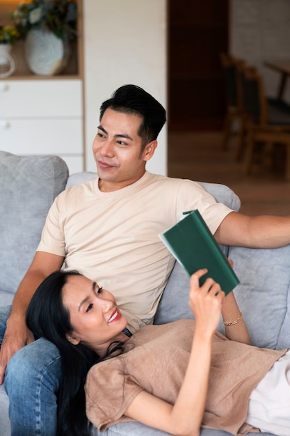 Affectionate couple at home on the couch reading book and having a drink