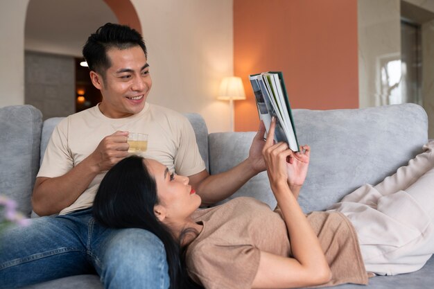 Free photo affectionate couple at home on the couch reading book and having a drink