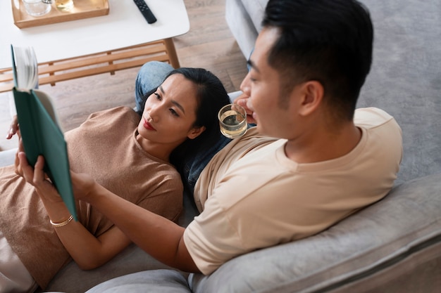 Affectionate couple at home on the couch reading book and having a drink