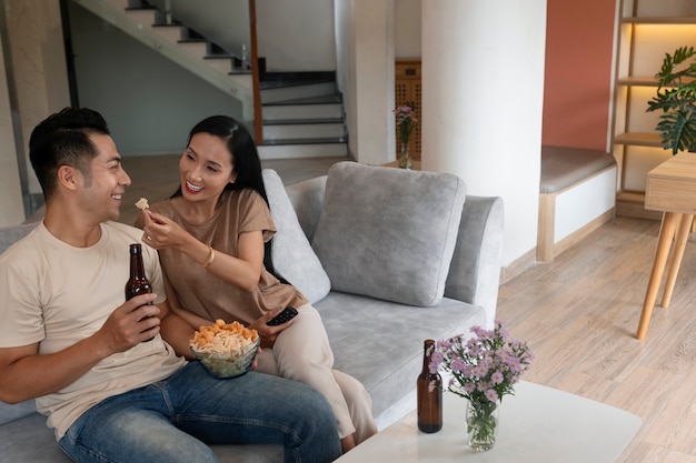Affectionate couple at home having food in bowl and beer