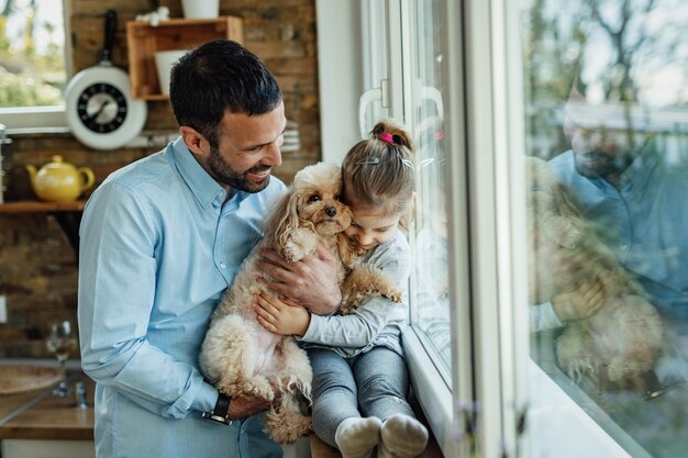 아버지와 함께 창가에서 휴식을 취하는 동안 개를 안고 있는 다정한 어린 소녀