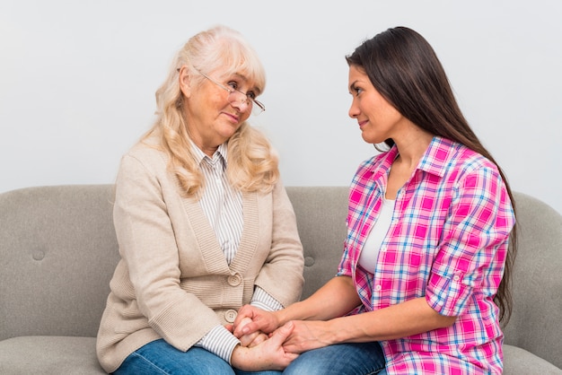 Affectionate mother and daughter looking at each other holding hands sitting on sofa