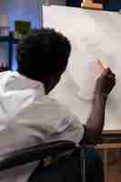 Foto gratuita artista afroamericano in sedia a rotelle che fa ombra usando la matita grafica che lavora all'illustrazione del vaso durante la lezione di pittura in studio d'arte. studente creativo con disabilità che disegna un'idea artistica
