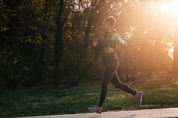 African American athletic woman running in the park during sunny autumn day Copy space