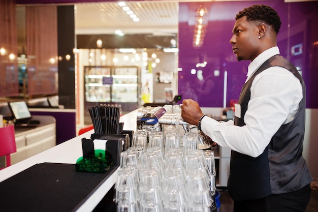 Barista afroamericano al bar che versa dal rubinetto birra fresca nel bicchiere del pub