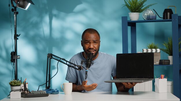 African american blogger doing product review of laptop on camera while recording for vlog channel. Black vlogger reviewing gadget on video for social media podcast. Man with device