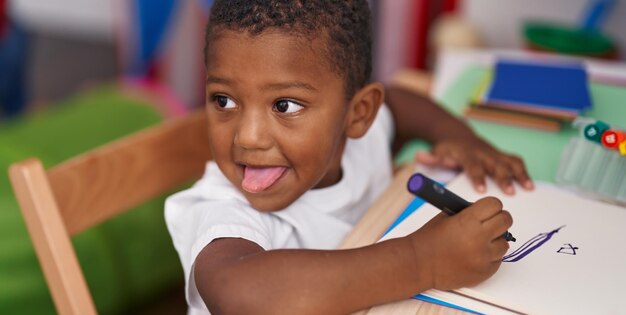 幼稚園でノートに絵を描くテーブルの上に座っているアフリカ系アメリカ人の少年