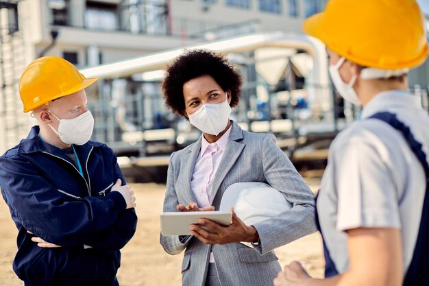 African American building contractor talking to civil engineers at construction site during coronavirus epidemic