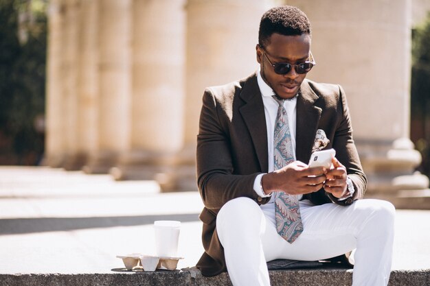 African american business with coffee and phone sitting on the stairs of a building