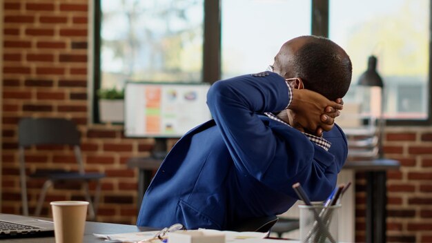 African american businessman relaxing laid back in office chair, taking work break after planning strategy during covid 19 pandemic. Sitting with hands behind head on job timeout.