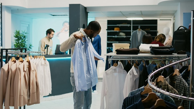 African american client examining fabric of formal shirts hanging in department store at mall. Male customer looking at trendy fashionable merchandise, buying modern clothes at shop.