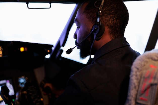 아프리카계 미국인 부조종사는 캡틴과 함께 조종석에서 비행기를 조종하고 레버와 전원 버튼을 사용하여 이륙합니다. 계기판 제어 명령 스위치를 눌러 비행하는 승무원. 확대.