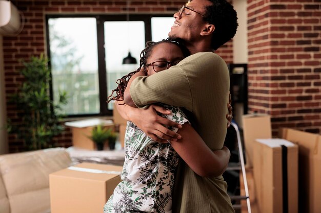 아프리카계 미국인 부부는 새 집으로 이사한 후 포옹을 나누고 재산 이전을 즐기고 낭만적인 순간을 보내고 있습니다. 임대 아파트에서 인생 이벤트를 포옹하고 축하합니다.